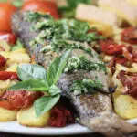 oven baked grey mullet served with potatoes, vegetables, garlic sauce and garnished with fresh basil leaf